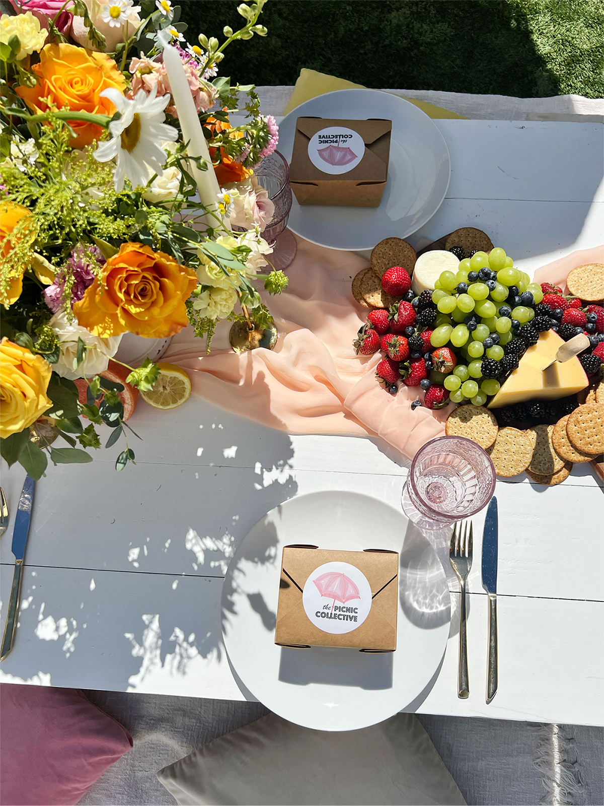Flowers and fruit on a table accented with candles and colorful glassware.