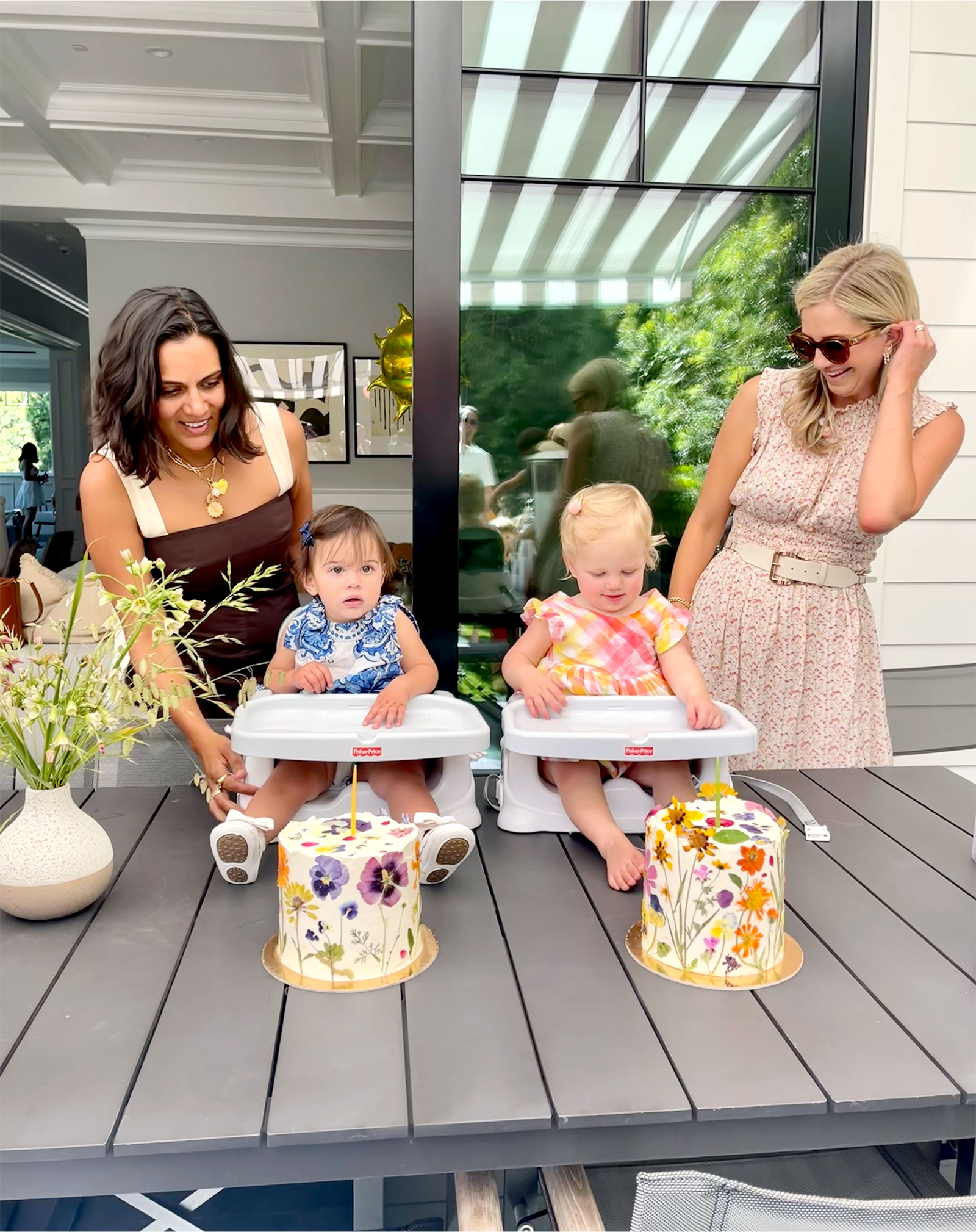 Two little girls with their moms sitting in front of cakes.