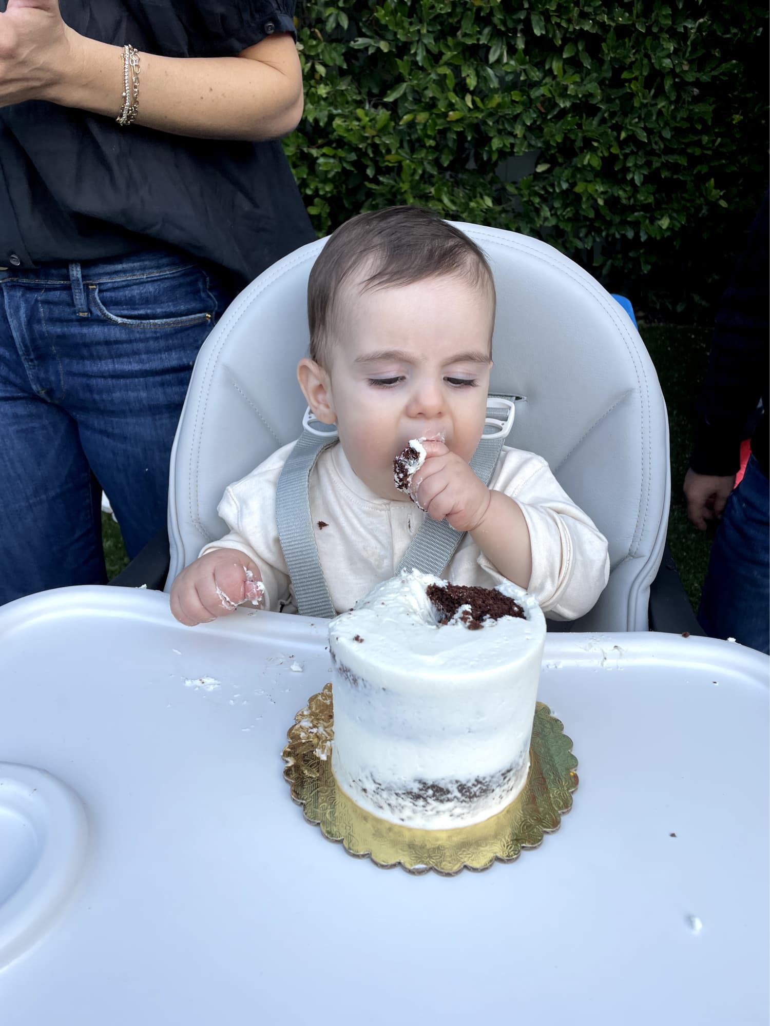 Baby in high chair eating cake with his hands.