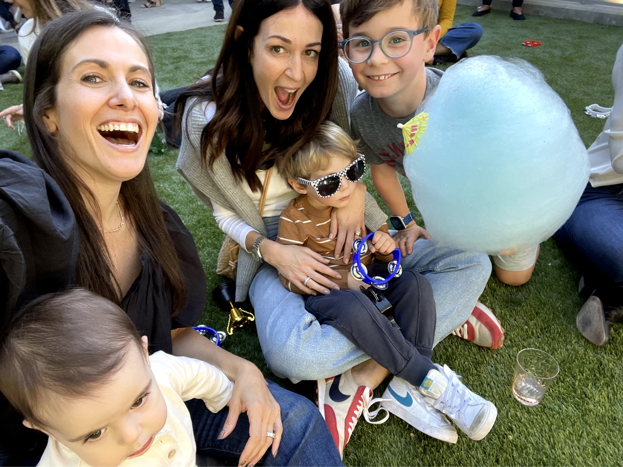 Parents sitting on the ground posing with their children. One child holds a big, blue cotton candy.