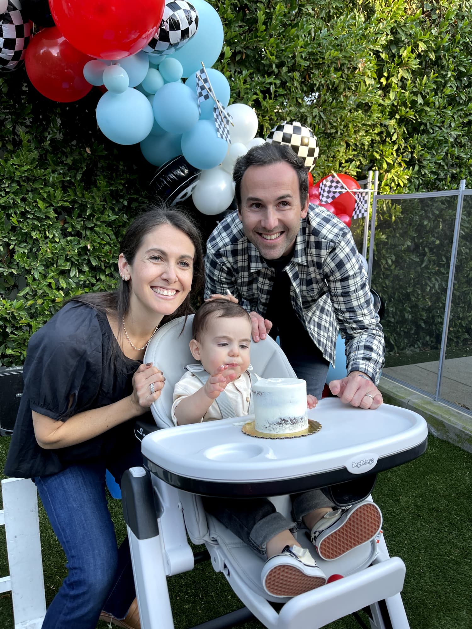 The birthday boy sits in a high chair as his parents pose behind him.