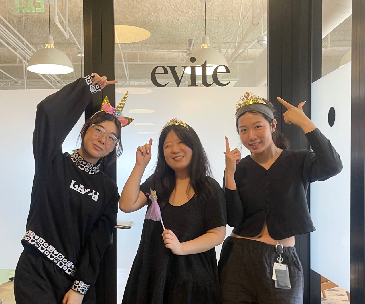 Three girls pose in front of a sign that says "Evite."