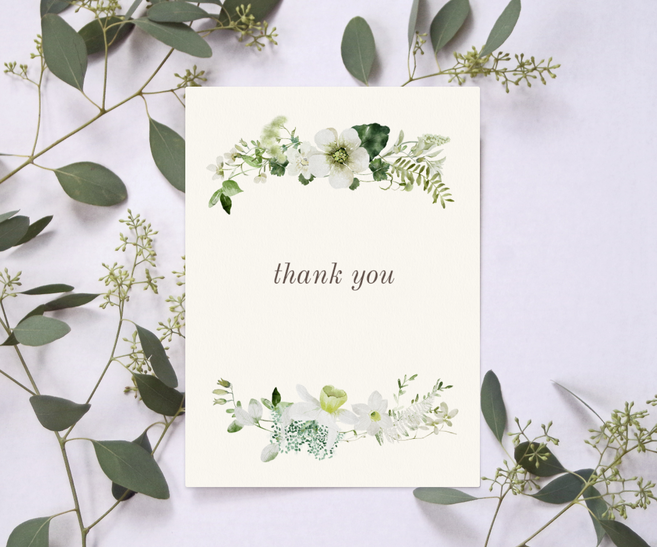 Green and white floral thank you card on a white background with sprigs of greenery surrounding it.