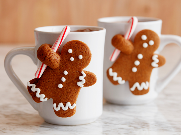 Gingerbread men hanging from a cup of hot chocolate.